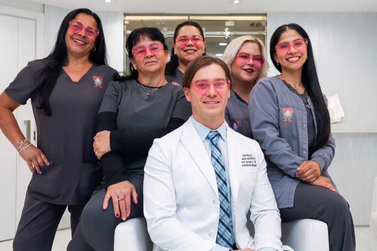Dr. Kroum Dimitrov, a board-certified oral surgeon, and his dental team at Love Your Jaws Surgery Center in South Miami smiling in pink safety glasses.