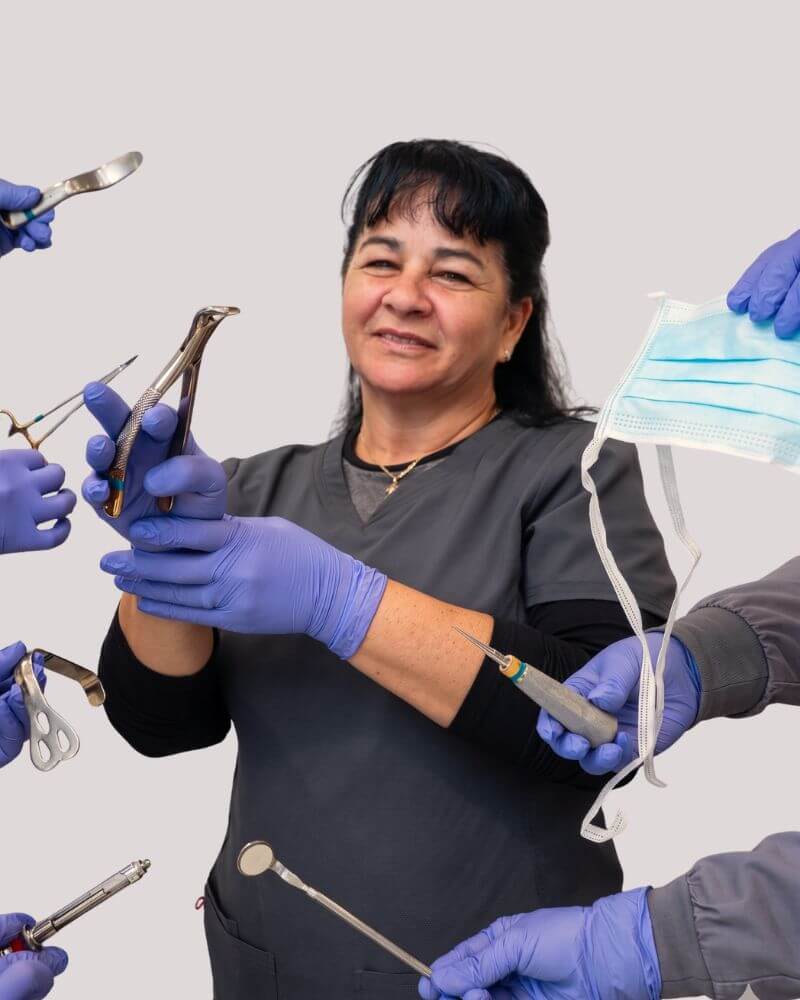 A smiling surgical assistant at Love Your Jaws Surgery Center in South Miami wearing grey scrubs and blue gloves, holding dental extraction forceps among hands displaying various oral surgery instruments and a blue medical mask.