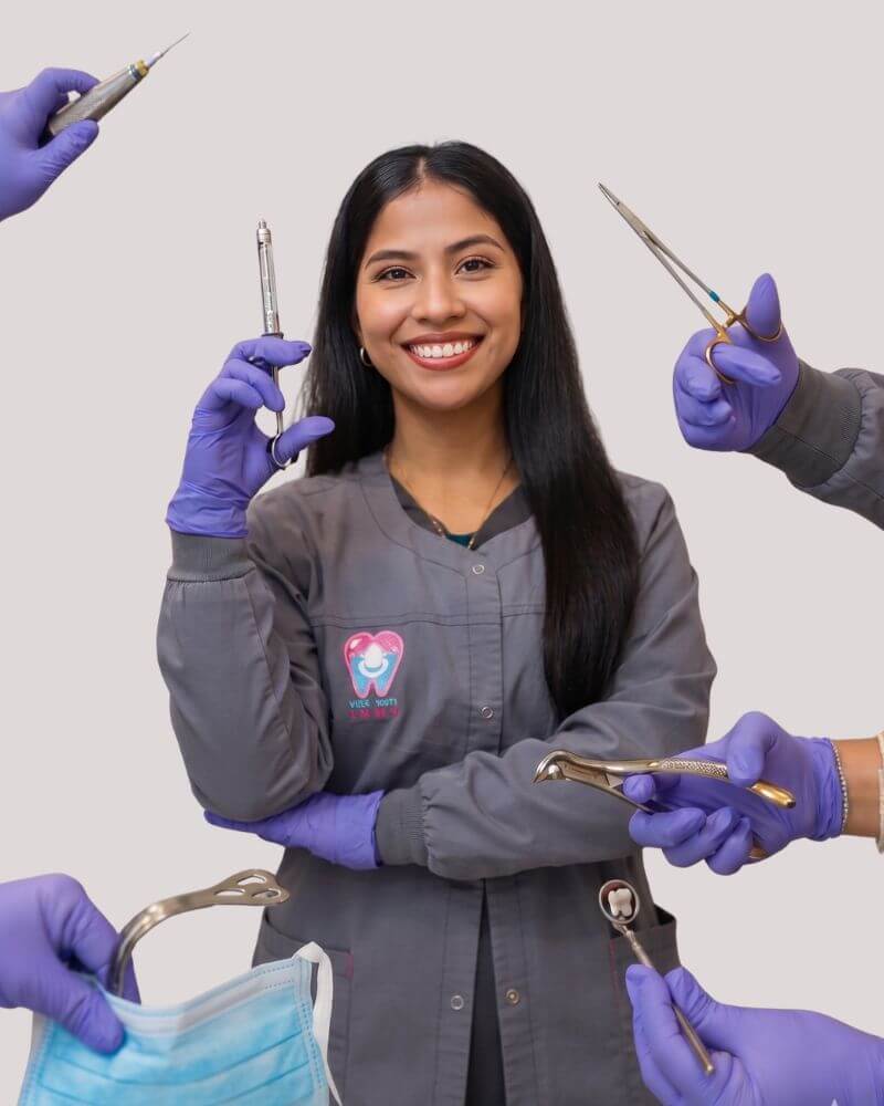 A smiling female surgical assistant in grey scrubs at Love Your Jaws Surgery Center in South Miami, holding a syringe and surrounded by gloved hands holding various dental surgical instruments.