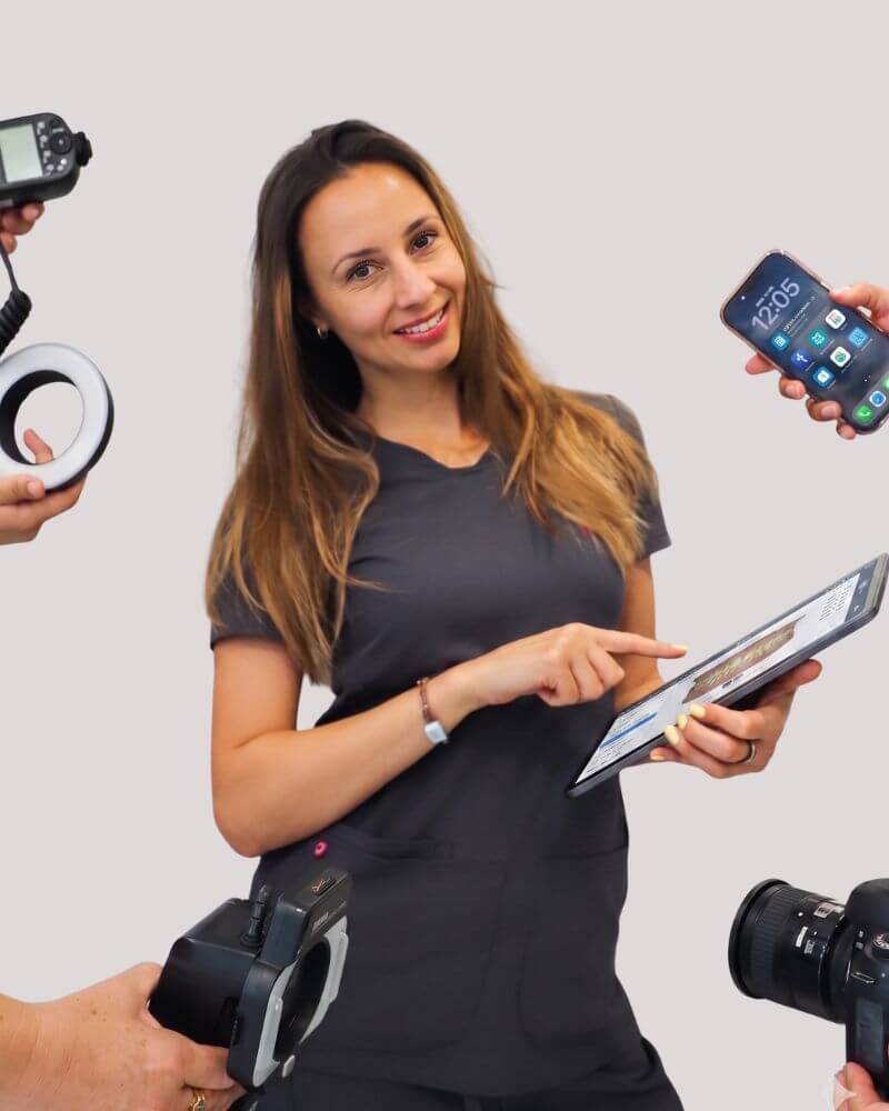 A smiling marketing manager at Love Your Jaws Surgery Center in South Miami wearing grey scrubs, pointing at a digital tablet and surrounded by hands holding a camera, smartphone, and photography lighting equipment.